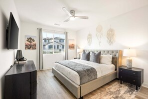 Ein Schlafzimmer mit Bett, Nachttischen, Deckenventilator und Kunstwerken an den Wänden.