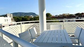 Un balcone con tavolo e sedie, affaccia su una città con edifici e una montagna.