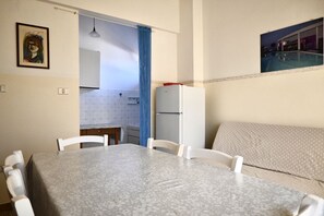 Une cuisine de taille réduite comprenant une table à manger, des chaises, un réfrigérateur et un rideau bleu.