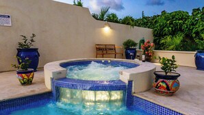 Un bain à remous doté d’une cascade, entouré de plantes en pot et agrémenté d’une chaise en bois.