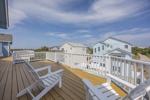 A wooden deck with white railings and chairs, overlooking a row of light blue houses with white trim. - 1892 - Carolina Bliss - Large Corolla Escape | Sleeps 30, Pool & Beach (Corolla)