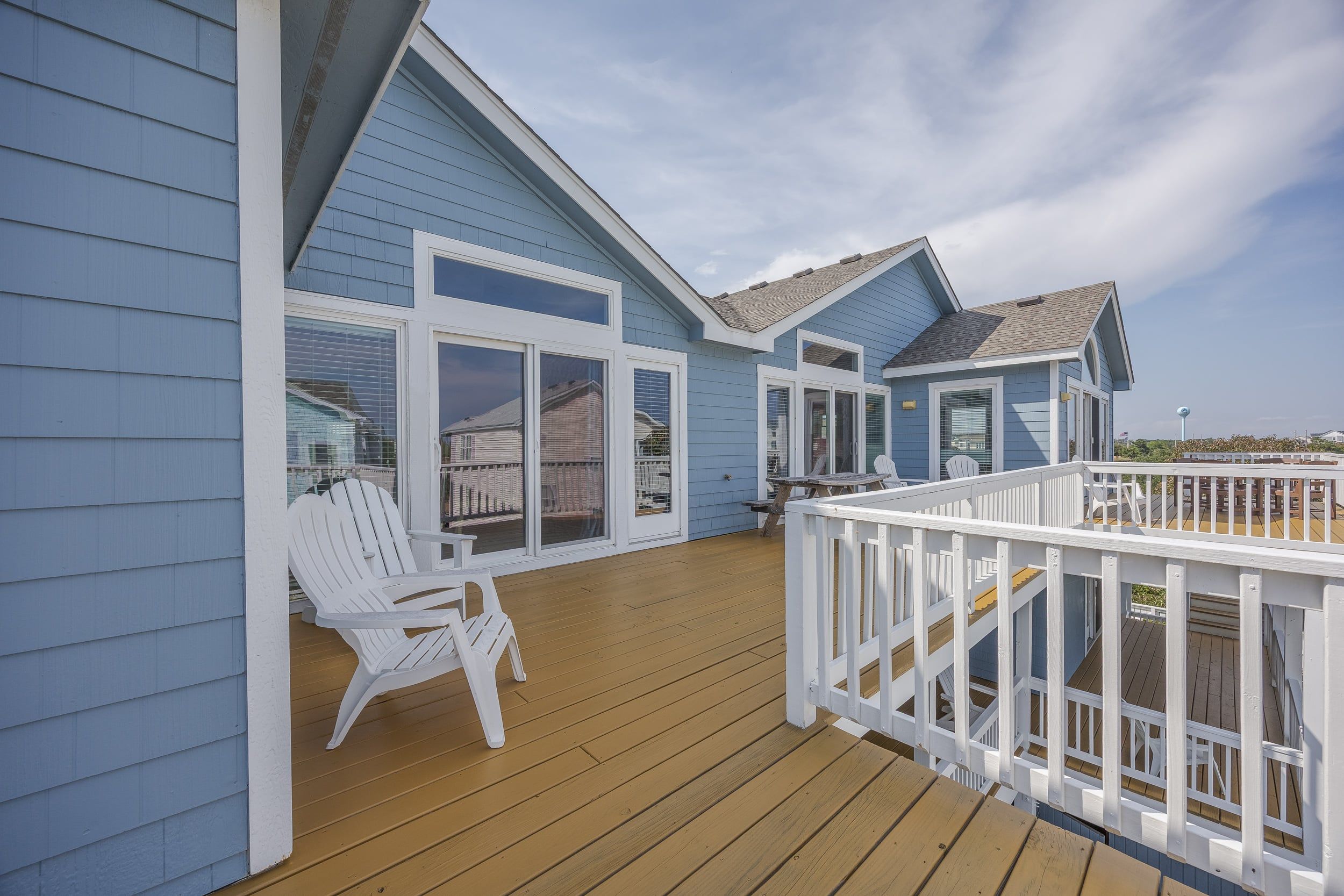 A blue building with a wooden deck, white railings, and a clear sky.