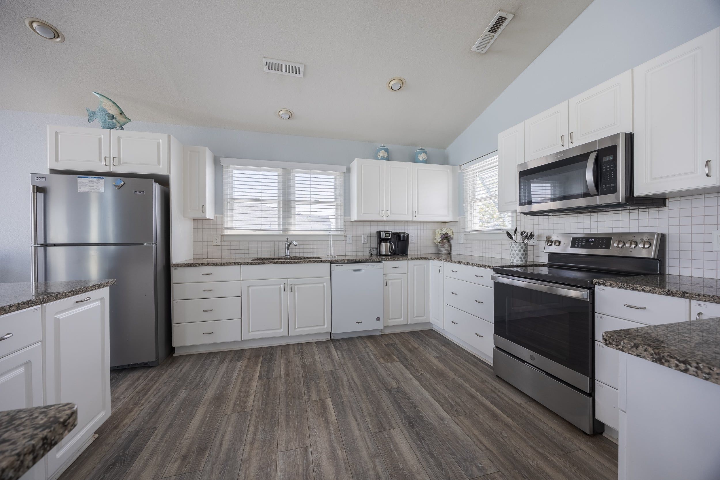 A modern kitchen with white cabinetry, stainless steel appliances, and a wooden floor.