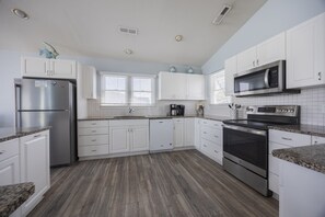 Une cuisine moderne avec des meubles blancs, des appareils électroménagers en acier inoxydable et un plancher en bois.