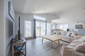 Un vaste espace de vie comprenant un téléviseur à écran plat, une table basse en bois et un canapé beige.