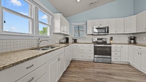 Una cocina moderna con armarios blancos, encimeras de granito, horno de acero inoxidable y una ventana con persianas.