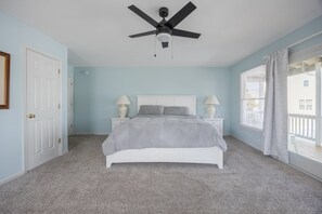 A bedroom with a bed, two bedside lamps, a ceiling fan, a white door, and a window with blinds.