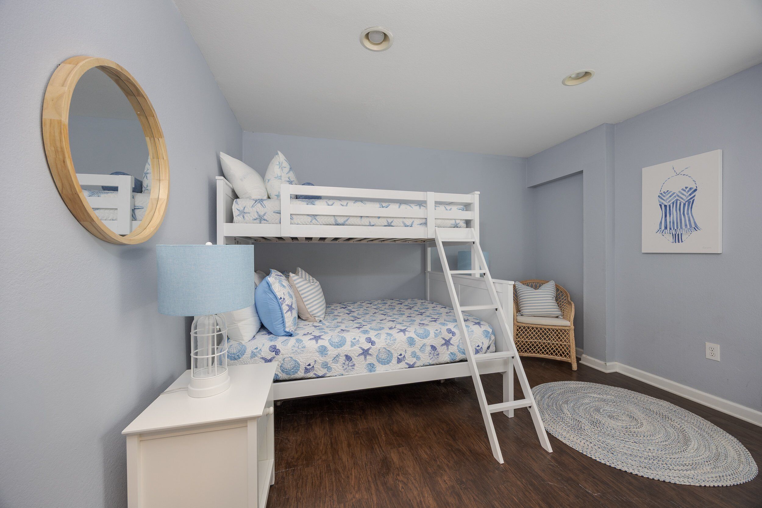 A bunk bed with a ladder, a bedside table with a lamp, a round mirror, and a woven rug.