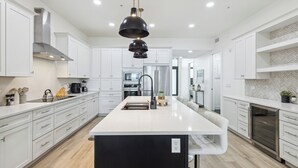 A modern kitchen with white cabinetry, a central island, stainless steel appliances, and pendant lighting. - Sleek Coastal Condo with Stunning Riverfront Views and Luxury Amenities (Melbourne Beach)