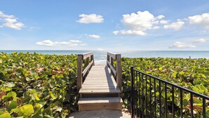 A wooden boardwalk leading to the beach, surrounded by green vegetation. - Sleek Coastal Condo with Stunning Riverfront Views and Luxury Amenities (Melbourne Beach)