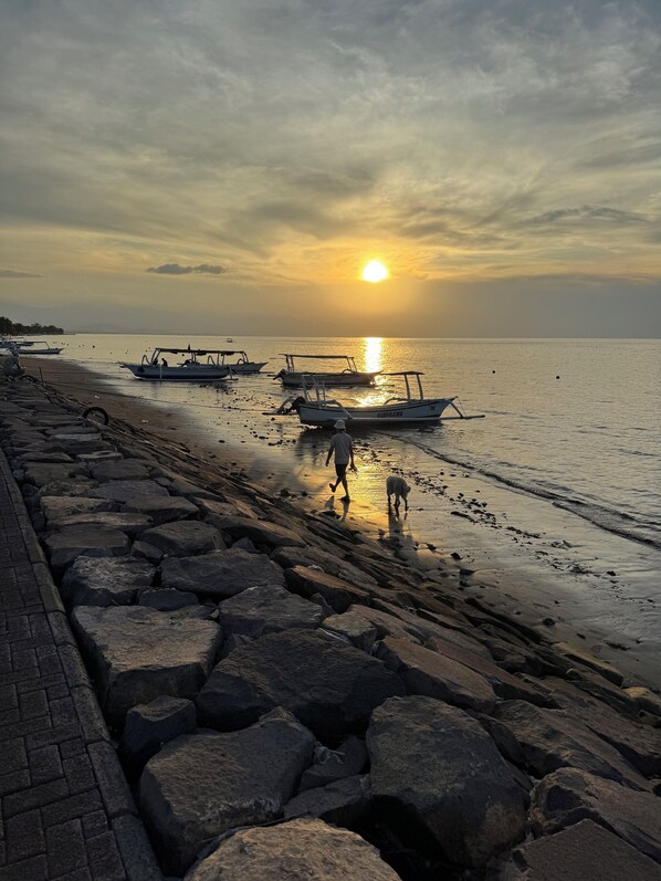 A beach with boats and a person walking a dog. - Rumi Bumi Lovina (Buleleng)