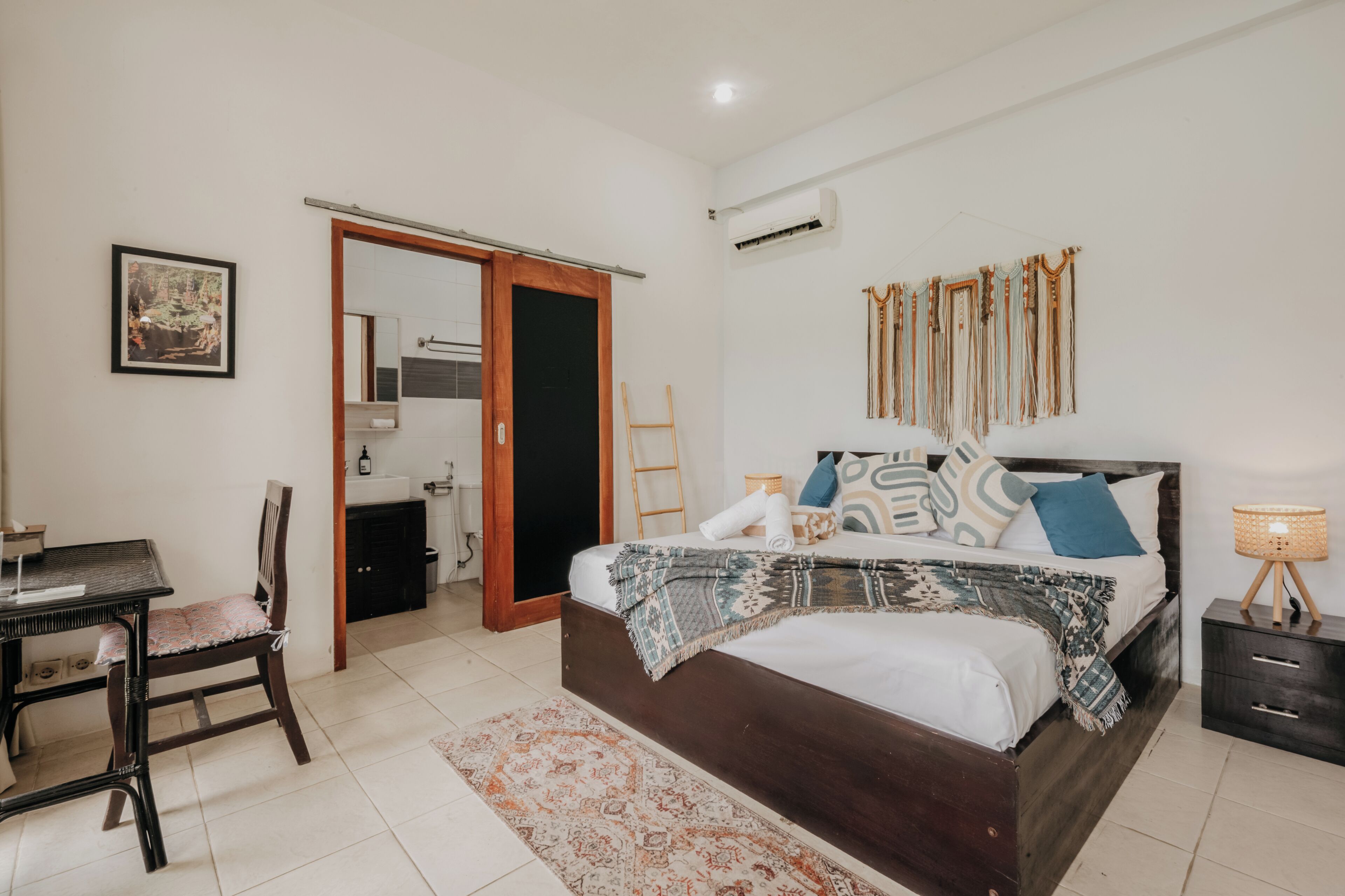 A bedroom with a bed, bedside table, chair, and a small desk.
