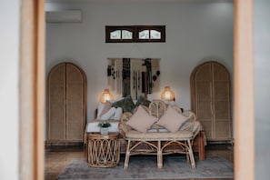 A room with a bed, two wicker chairs, a wall-mounted tapestry, and a hanging light fixture. - Rumi Bumi Lovina (Buleleng)