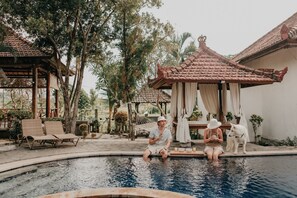 A pool area with a gazebo, lounge chairs, and a dog. - Rumi Bumi Lovina (Buleleng)
