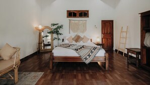 Un dormitorio con una cama de madera, un espejo grande, un tapiz de macramé en la pared y una puerta de madera.