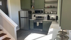 Een moderne keuken met groene kastjes, roestvrijstalen apparatuur en een wit aanrecht.