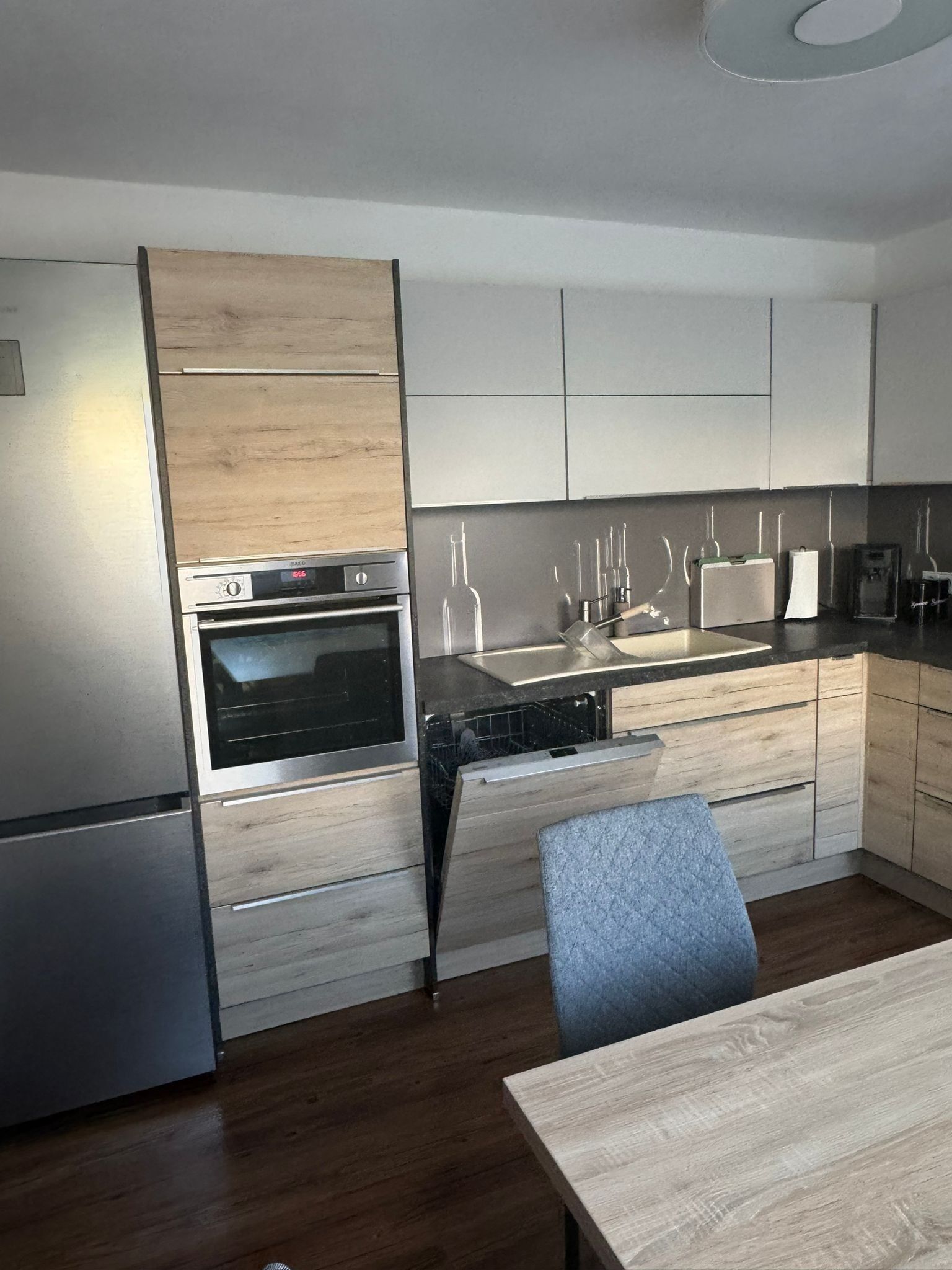 A modern kitchen with a built-in oven, a sink, and a dining area with a table and chairs.