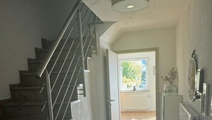 A staircase leading to a second floor, a hallway with wooden flooring, a radiator, and a window with a view of greenery.