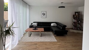 A modern living room with a wooden floor, a black leather sofa, a wooden coffee table, and a bookshelf.