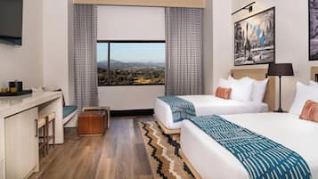 Habitación de hotel con dos camas, un escritorio, una silla, una mesita, una lámpara y un cuadro en la pared.