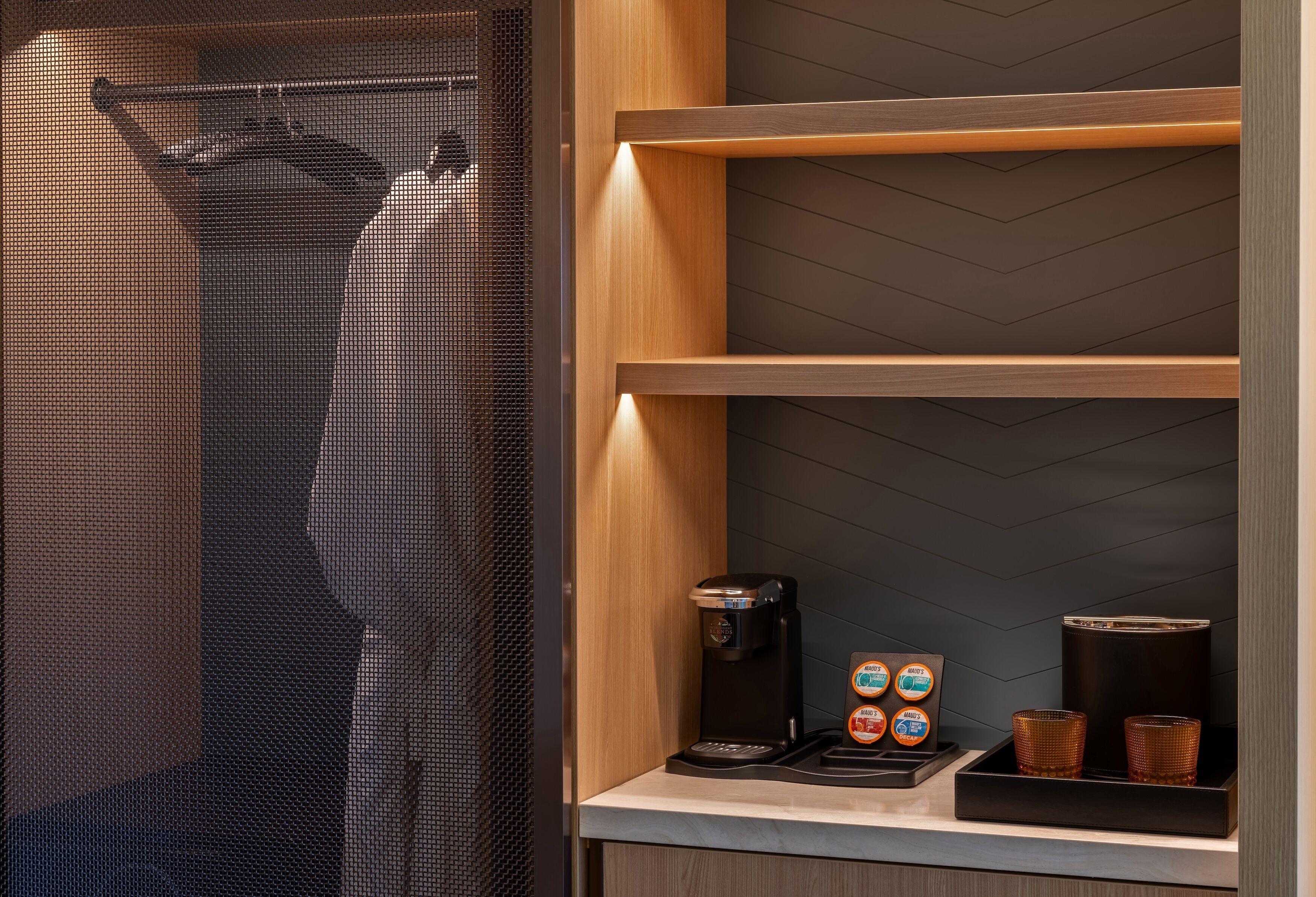 Et moderne badeværelse med bruseområde, kaffemaskine og en hylde med toiletartikler.