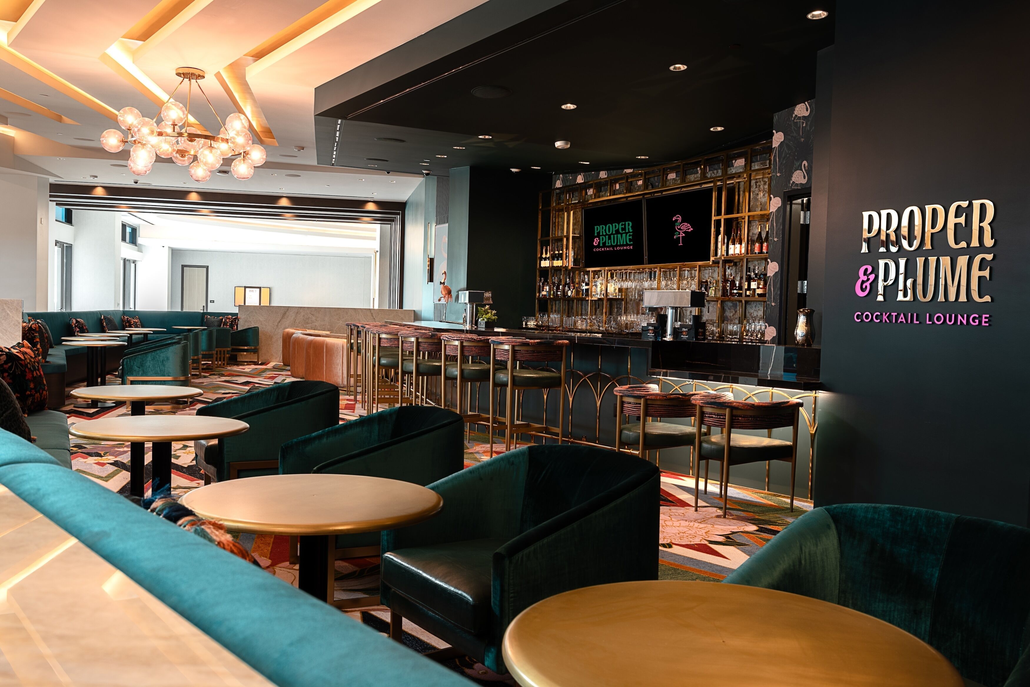 A modern lounge with teal sofas, round tables, and a bar area.
