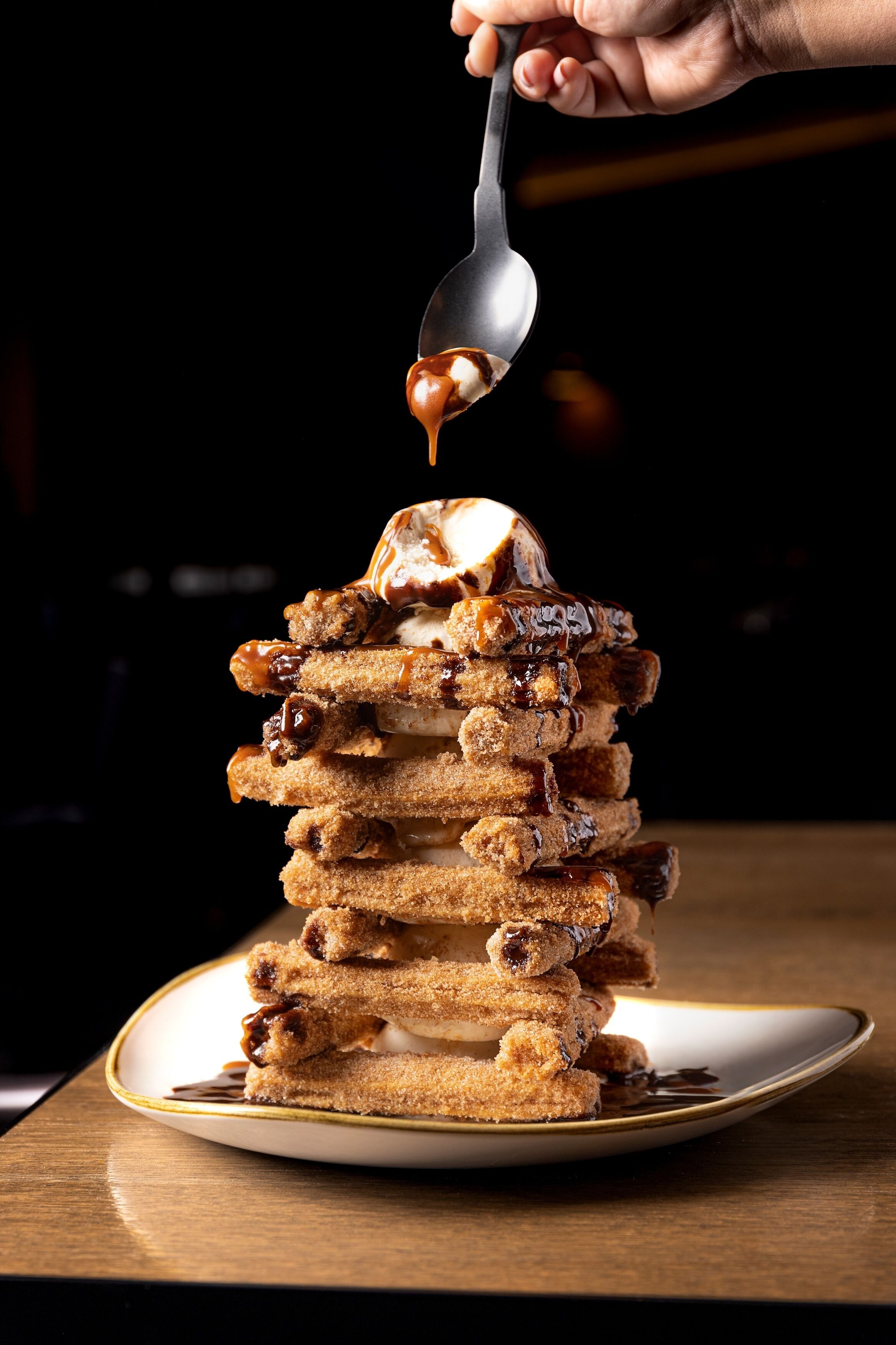 A stack of churros with chocolate sauce being poured over them.