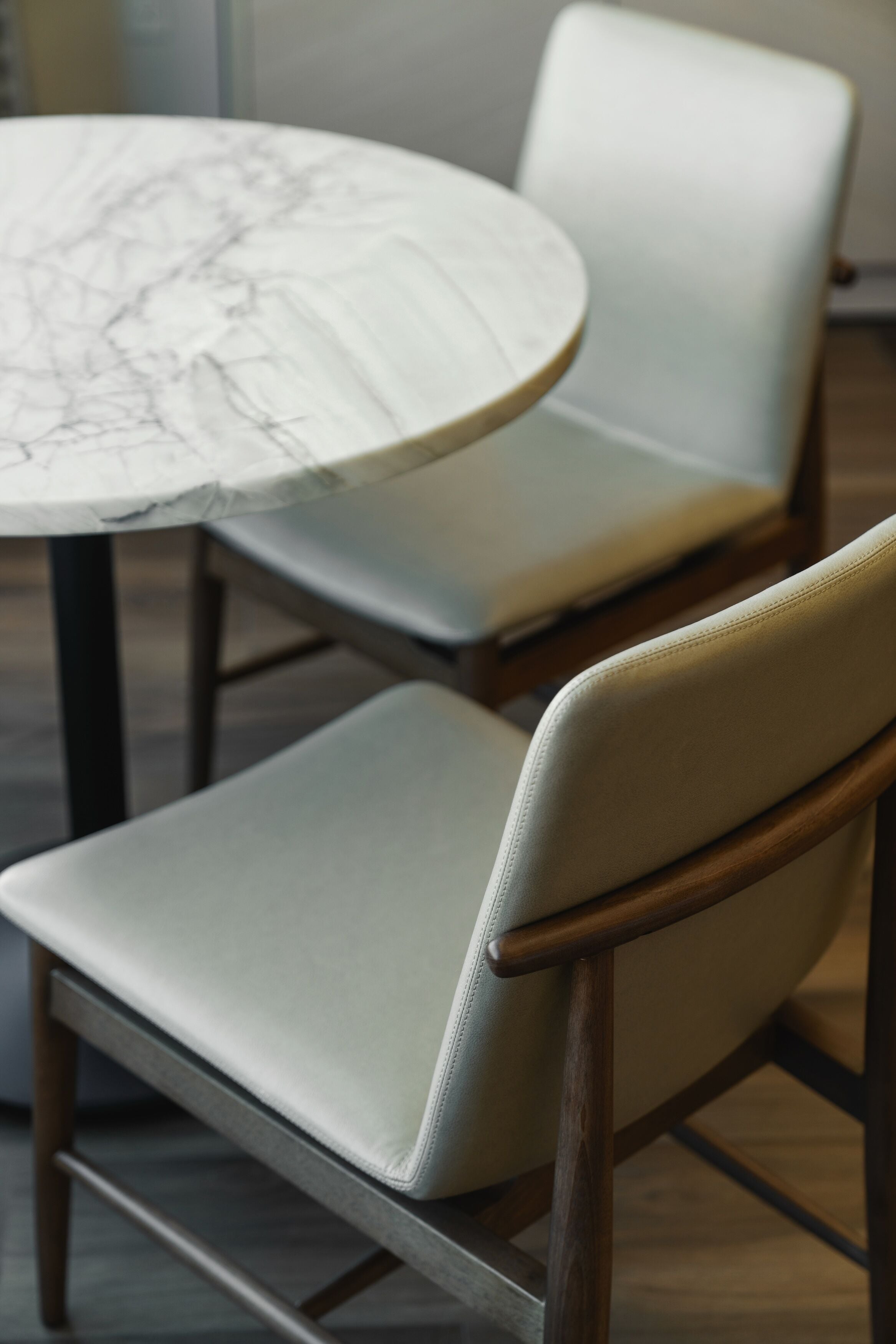 A round table with a marble-like surface and two upholstered chairs with wooden legs.