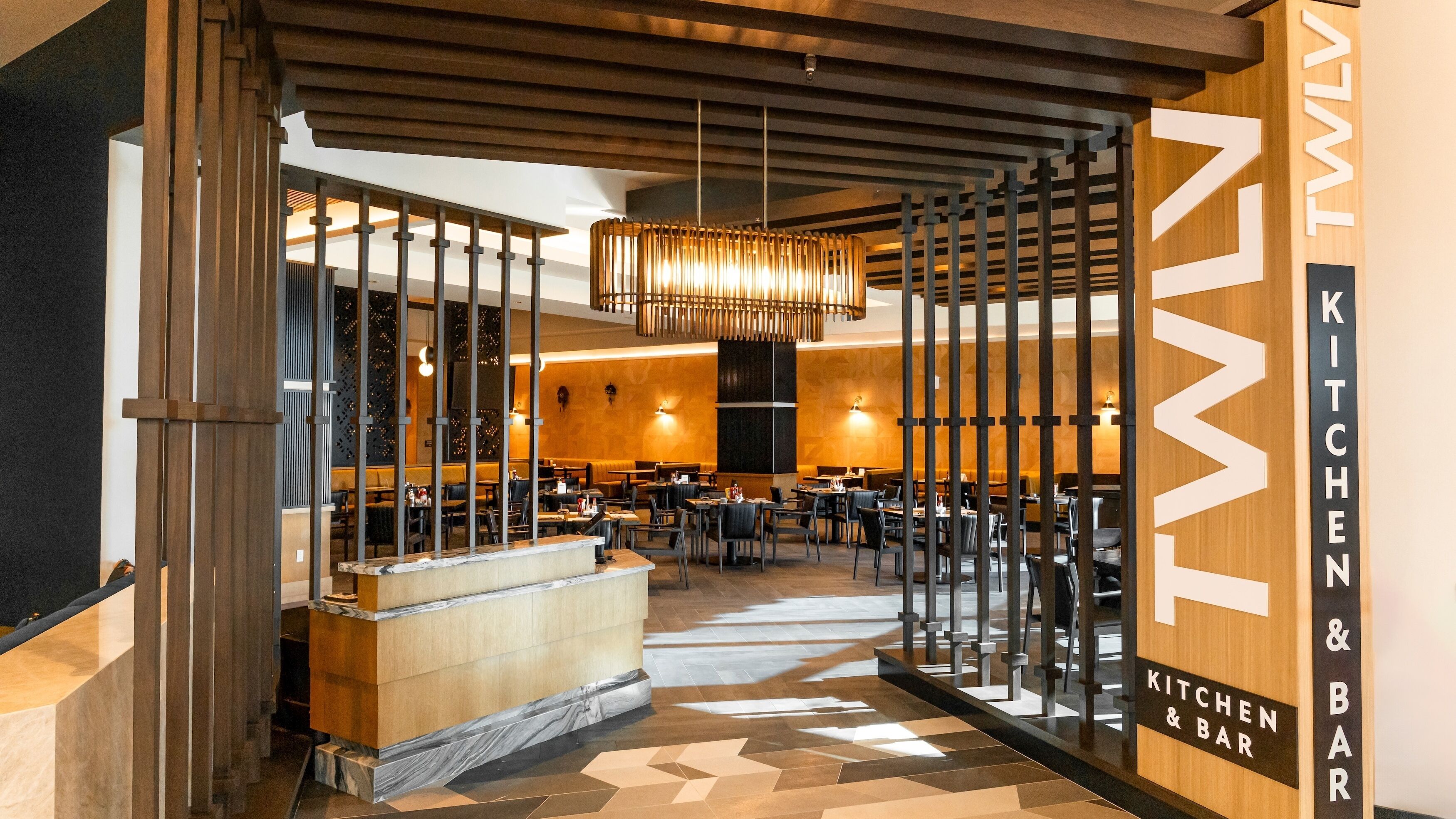 En modern restaurang med en central bardisk, trädetaljer och ett geometriskt mönster på golvet.