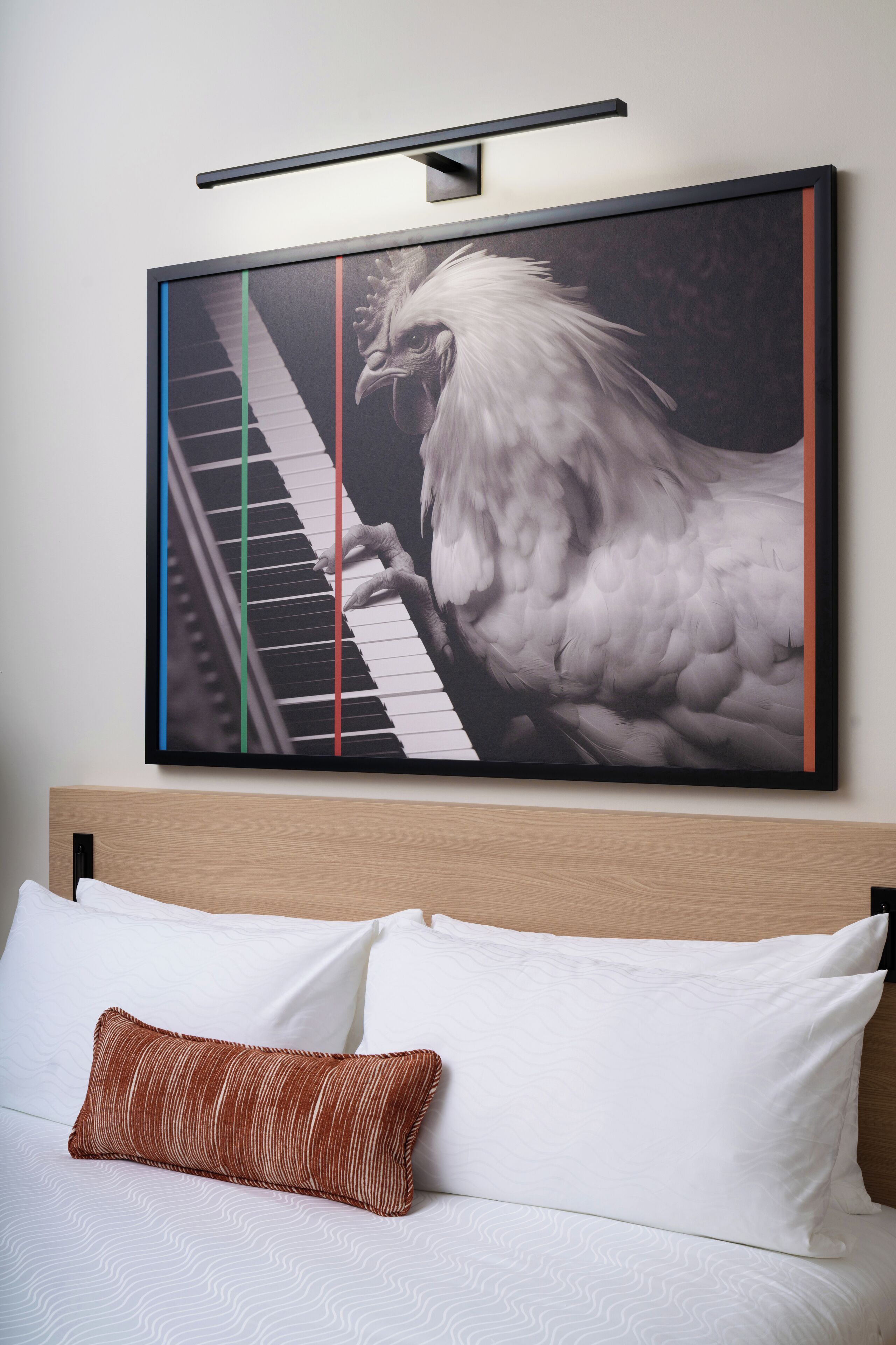 Hotelkamer met een groot gekaderd kunstwerk van een vogel die piano speelt, een houten hoofdeinde en een geborduurde sprei.