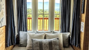 A cozy cabin room with a built-in bench and cushions, large windows with curtains, and a wooden ceiling. - Charming Tiny House with Breath-Taking Views in Delano, TN (Delano)