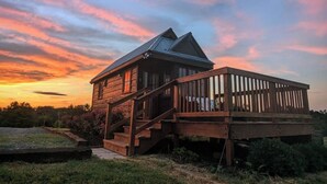 A wooden cabin with a metal roof, a wooden deck, and a staircase leading to a covered porch. - Charming Tiny House with Breath-Taking Views in Delano, TN (Delano)