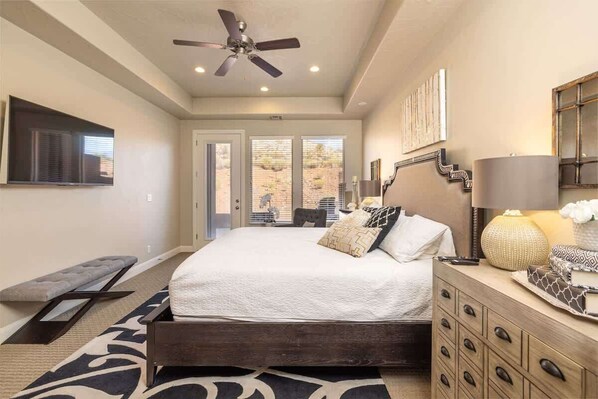 A bedroom with a bed, a bench, a dresser, a ceiling fan, and a view of the outdoors.