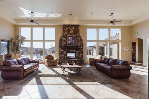 A spacious living area with a stone fireplace, leather sofas, and large windows offering a view.