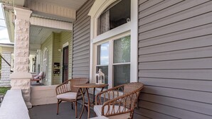 Eine Veranda mit Korbstühlen und einem kleinen Tisch, eine weiße Säule und ein Fenster mit Blick auf das Haus.