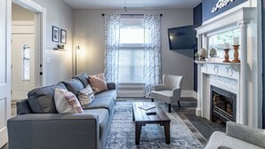 Ein Wohnzimmer mit Sofa, Sesseln, Couchtisch, Kamin und Deckenventilator.