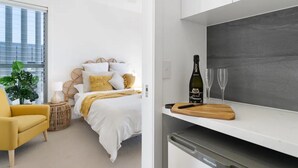 A modern bedroom with a bed, bedside table, and a potted plant. - Oceanviews on Pearl (Kingscliff)