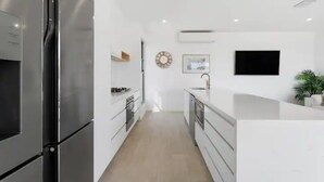 A modern kitchen with white cabinetry, a built-in oven, and a stainless steel refrigerator. - Oceanviews on Pearl (Kingscliff)