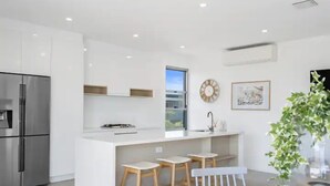 A modern kitchen with a central island, bar stools, and a dining table. - Oceanviews on Pearl (Kingscliff)