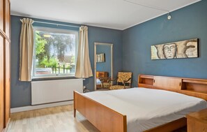 A bedroom with a bed, a chair, a wooden nightstand, a mirror, and a window with curtains. - Cozy home in Bandholm with WiFi (Bandholm)