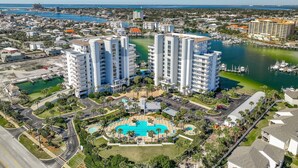 A high-rise hotel with a central swimming pool, surrounded by greenery and a marina. - Harbor Landing 102B- The heart of Destin: shopping & restaurants! Beach access w/ pools & hut tubs! (Destin)