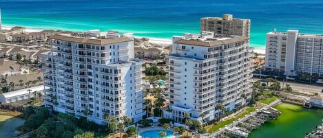 Un hotel moderno de gran altura con varios balcones, un puerto deportivo y vista a la playa.