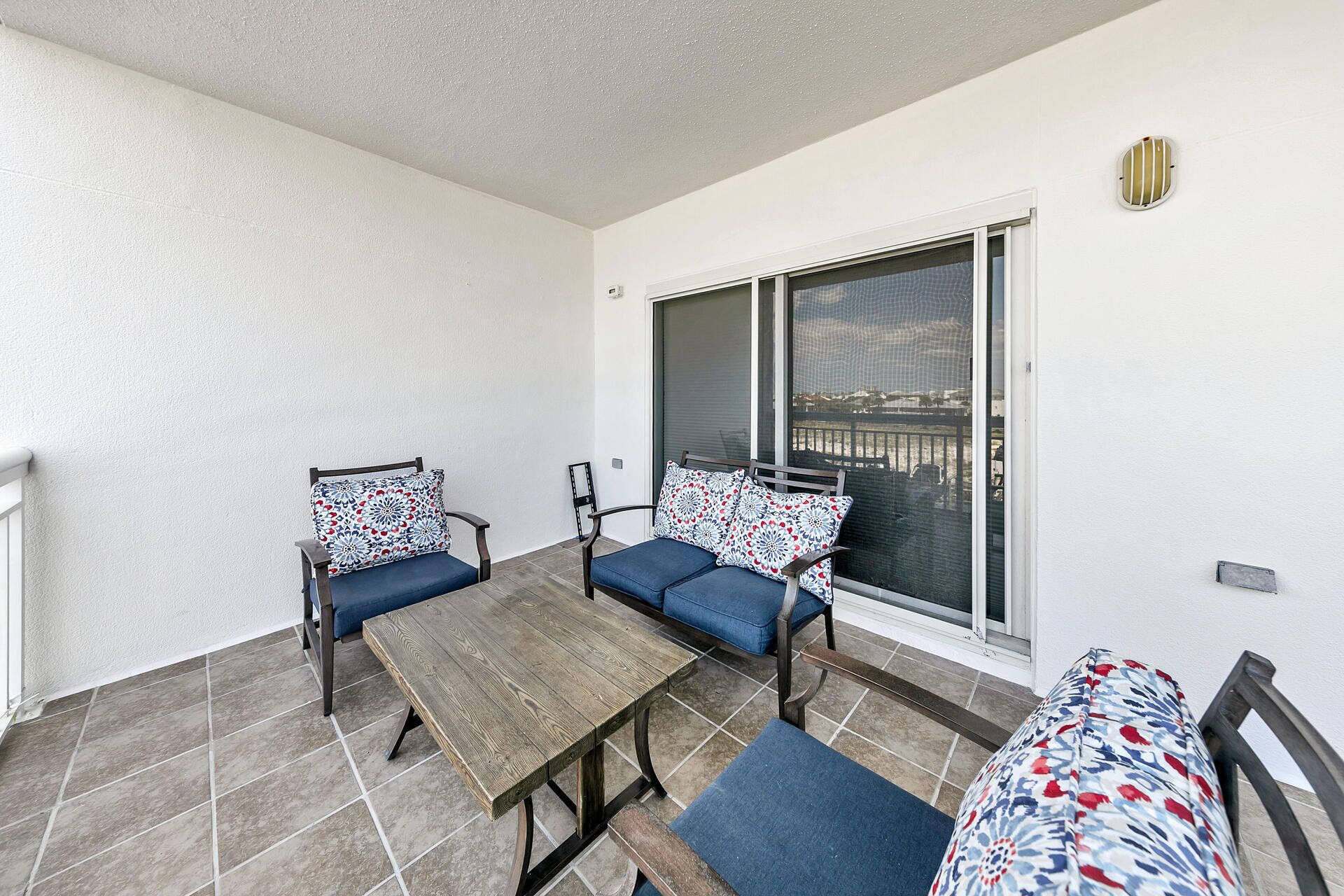 Un balcon avec une table en bois, deux chaises et un canapé, le tout agrémenté de coussins à motifs.