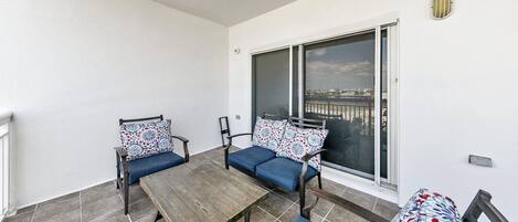 Un balcon avec une table en bois, deux chaises et un canapé, le tout agrémenté de coussins à motifs.