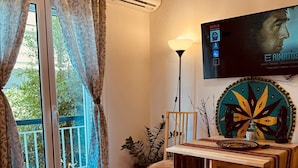 Une pièce comprenant un lit, une table ornée d’une assiette décorative, une chaise, une plante en pot et un téléviseur fixé au mur qui diffuse un film.