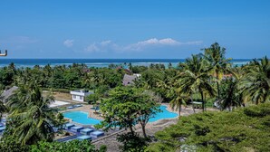 A resort with a swimming pool, palm trees, and a view of the ocean.