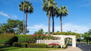 Una entrada ajardinada con palmeras, un letrero que dice "The Palms", y un cielo despejado.