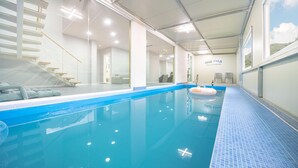 Een binnenzwembad met helderblauw water, een betegelde rand en een glazen wand aan één kant.