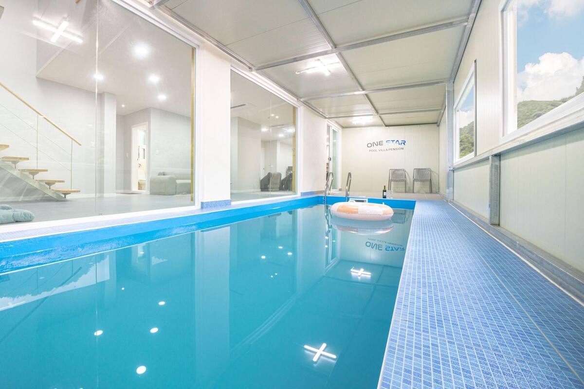 En indendørs swimmingpool med krystalklart, blåt vand, en fliset kant og en glasvæg på den ene side.