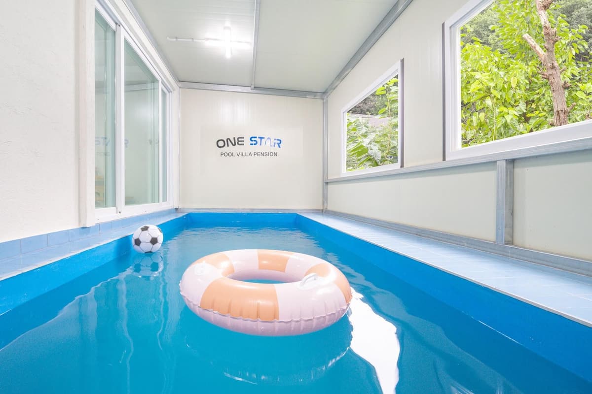 En swimmingpool med blå interiør, en hvid væg med skilt og et vindue med udsigt til grøn vegetation.